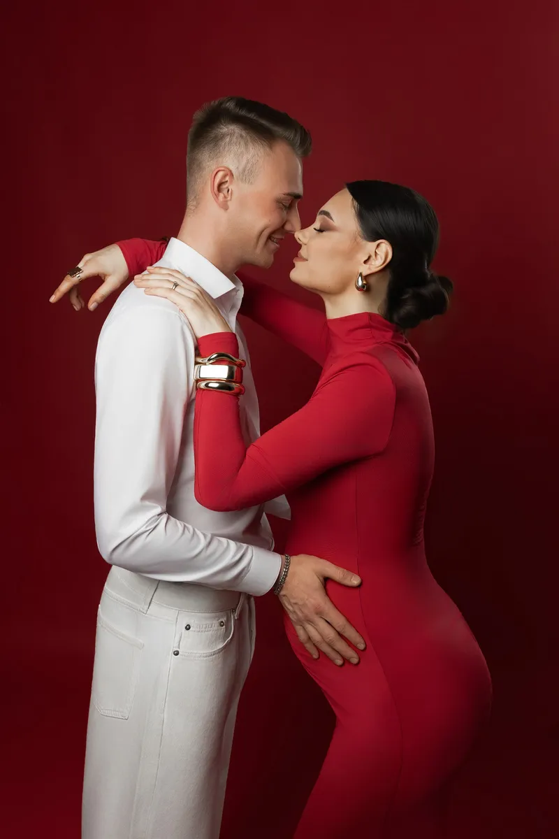 Ein Paar in einem roten Studio posiert für ein Babybauch-Shooting.