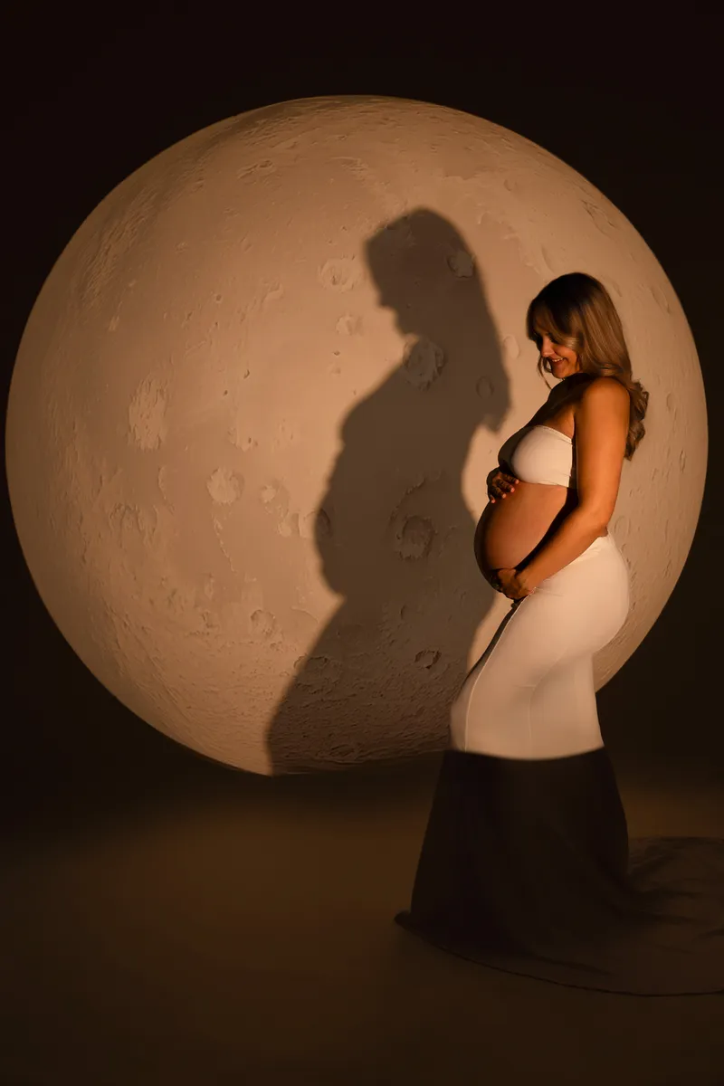 Eine schwangere Frau posiert vor einem großen Mond im Studio.